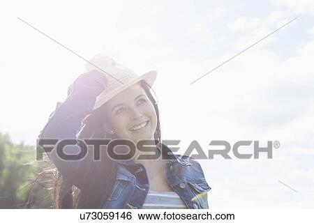 Stock Photograph - Young woman smiling, holding onto hat. Fotosearch