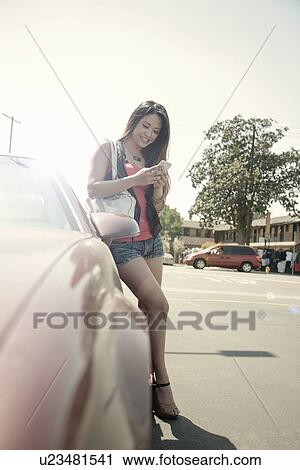 Young woman standing beside car, using smart phone View Large Photo Image Stock Image - Young woman standing beside car, using smart phone. Fotosearch