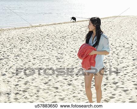 Stock Image - Young woman strolling on beach holding beach towel, Port Melbourne, Melbourne, Victoria, Australia. Fotosearch