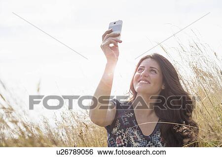 Stock Photograph - Young woman taking selfie with smartphone in field. Fotosearch