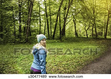 Stock Photo - Young woman walking in forest looking back over her shoulder. Fotosearch