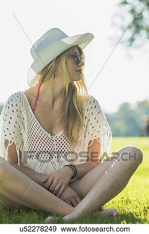 Stock Photo - Young woman wearing white sunhat sitting cross legged. Fotosearch