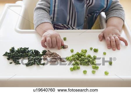 Stock Image - Baby girl (12-17 months) eating steak, spinach and green peas. Fotosearch