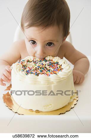 Stock Image - Baby girl (12-17 months) eating birthday cake. Fotosearch