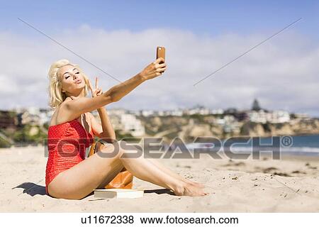 Stock Photo - Blond woman taking selfie on beach. Fotosearch