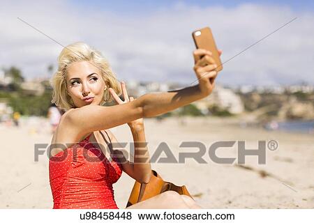 Stock Photo - Blond woman taking selfie on beach. Fotosearch