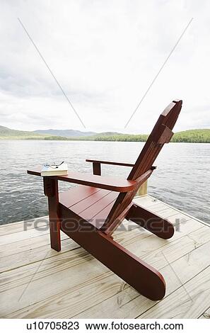 Stock Image - Book and chair on lake side dock. Fotosearch