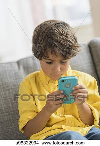 Boy (6-7) sitting on sofa and using cell phone View Large Photo Image Picture - Boy (6-7) sitting on sofa and using cell phone. Fotosearch
