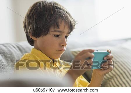 Boy (6-7) sitting on sofa and using cell phone View Large Photo Image Stock Photo - Boy (6-7) sitting on sofa and using cell phone. Fotosearch