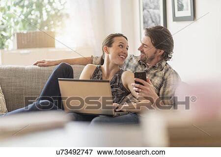 Cheerful couple on sofa with laptop and mobile phone View Large Photo Image Stock Photo - Cheerful couple on sofa with laptop and mobile phone. Fotosearch