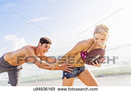 Cheerful young couple playing football on beach View Large Photo Image Stock Photo - Cheerful young couple playing football on beach. Fotosearch