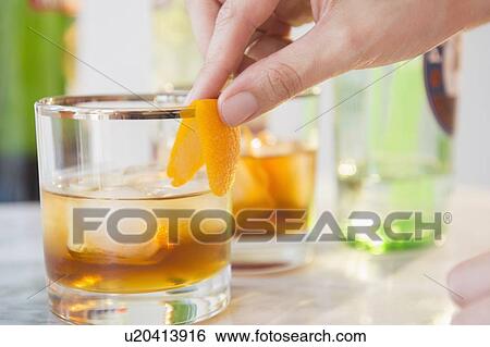 Stock Photograph - Close-up shot of bartender's hand decorating cocktail glass with orange peel. Fotosearch