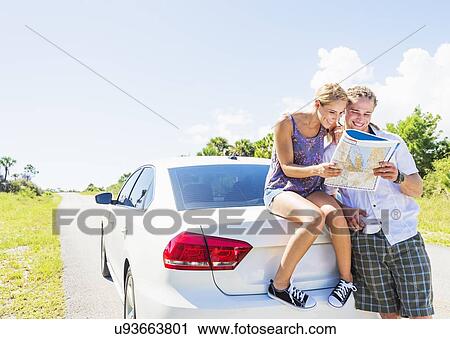 Stock Image - Couple at back of car looking at map. Fotosearch