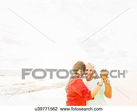 Stock Image - Couple dancing on beach at sunrise. Fotosearch