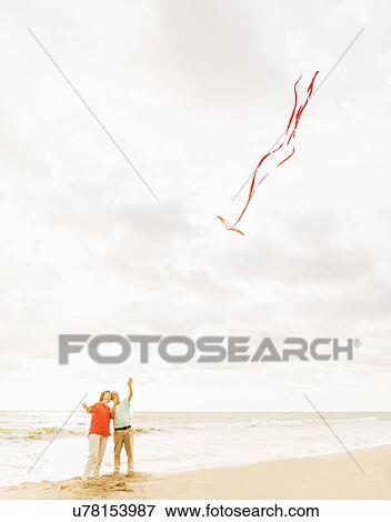 Stock Photo - Couple flying kite together on beach. Fotosearch