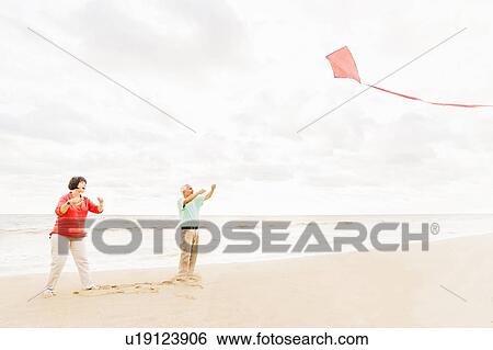 Stock Photograph - Couple flying kite together on beach. Fotosearch
