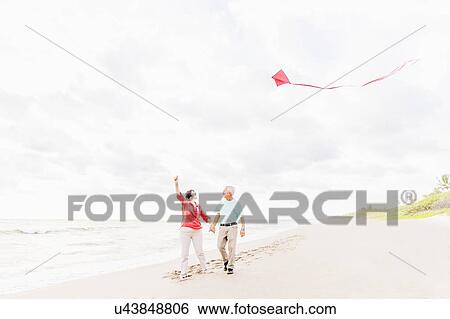 Couple flying kite together on beach View Large Photo Image Stock Photograph - Couple flying kite together on beach. Fotosearch