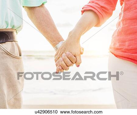 Stock Image - Couple holding hands on beach. Fotosearch
