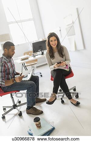 Couple sitting and working in office View Large Photo Image Stock Photo - Couple sitting and working in office. Fotosearch