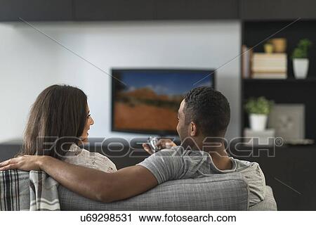 Stock Image - Couple sitting in living room and watching TV. Fotosearch