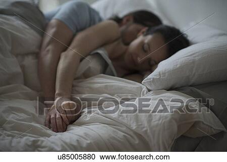 Stock Image - Couple sleeping together in bed at night. Fotosearch