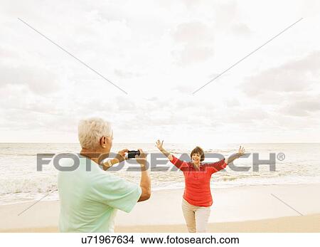 Picture - Couple taking pictures on beach at sunrise. Fotosearch