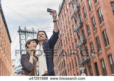 Couple taking selfie on street, Brooklyn Bridge in background View Large Photo Image Stock Photo - Couple taking selfie on street, Brooklyn Bridge in background. Fotosearch