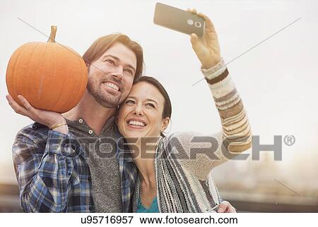 Couple taking selfie with mobile phone, man holding pumpkin View Large Photo Image Stock Photo - Couple taking selfie with mobile phone, man holding pumpkin. Fotosearch