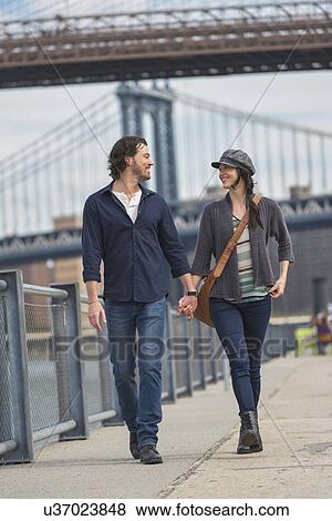 Couple walking on promenade, Brooklyn Bridge in background View Large Photo Image Stock Photo - Couple walking on promenade, Brooklyn Bridge in background. Fotosearch