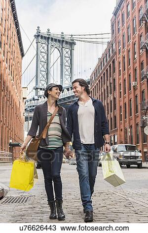 Stock Image - Couple walking on street, Brooklyn Bridge in background. Fotosearch