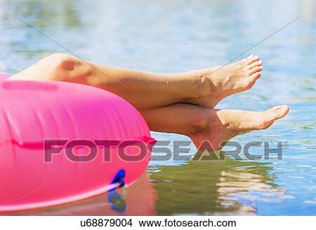 Picture - Cropped shot of legs of young woman floating on pink swim ring. Fotosearch
