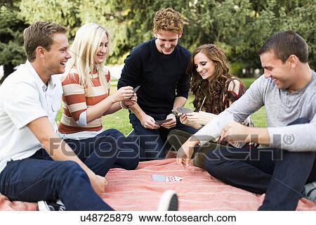 Stock Photo - Friends playing cards in park. Fotosearch