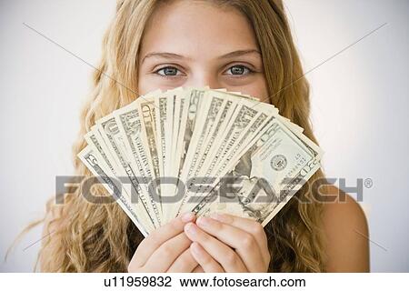 Stock Image - Girl (12-13) holding money fan against her face. Fotosearch