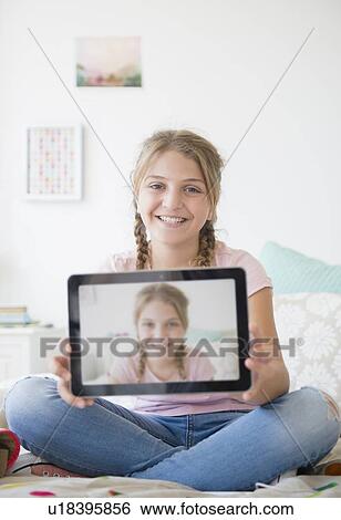 Stock Photograph - Girl (12-13) holding tablet with selfie. Fotosearch