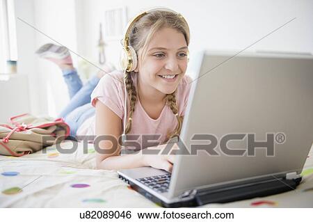 Girl (12-13) lying in bed using laptop View Large Photo Image Stock Photograph - Girl (12-13) lying in bed using laptop. Fotosearch