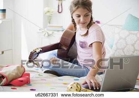 Stock Image - Girl (12-13) playing guitar and using laptop. Fotosearch