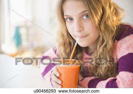 Stock Image - Girl (12-13) sipping carrot juice. Fotosearch
