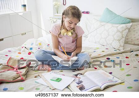 Stock Photo - Girl (12-13) sitting on bed doing homework. Fotosearch