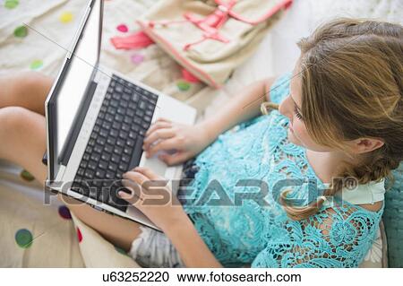 Stock Image - Girl (12-13) using laptop in bedroom. Fotosearch
