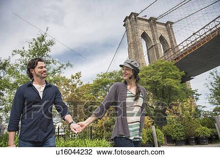Happy couple holding hands and walking with Brooklyn Bridge in background View Large Photo Image Stock Image - Happy couple holding hands and walking with Brooklyn Bridge in background. Fotosearch