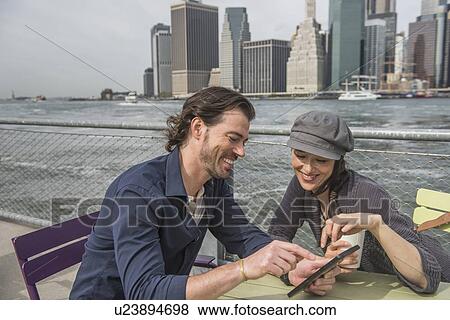 Stock Photo - Happy couple sitting and using tablet pc with cityscape in background. Fotosearch