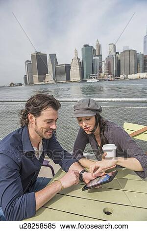Happy couple sitting and using tablet pc with cityscape in background View Large Photo Image Stock Photography - Happy couple sitting and using tablet pc with cityscape in background. Fotosearch