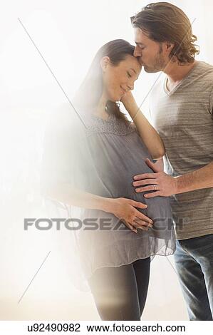 Stock Image - Man kissing pregnant woman. Fotosearch