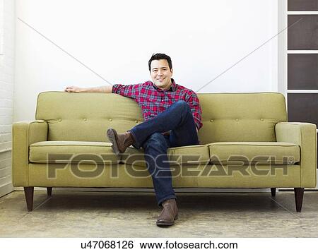 Stock Photograph - Man sitting on sofa and looking at camera. Fotosearch