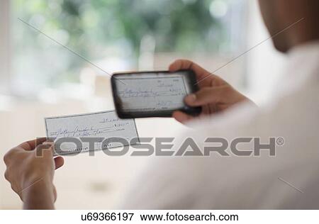Stock Photo - Man taking photo of banking check with cell phone. Fotosearch