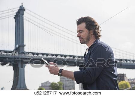 Stock Photo - Man using tablet pc, Manhattan Bridge in background. Fotosearch