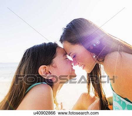 Stock Photograph - Mom and daughter (6-7) rubbing noses on sunny day on beach. Fotosearch