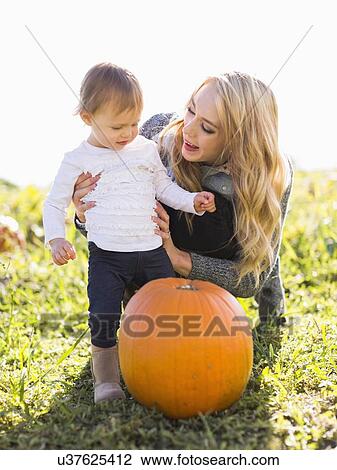 Stock Image - Mother and daughter (12-17 months) looking at large pumpkin. Fotosearch