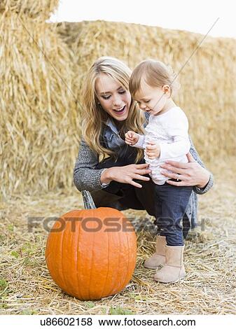 Stock Photo - Mother and daughter (12-17 months) looking at large pumpkin. Fotosearch