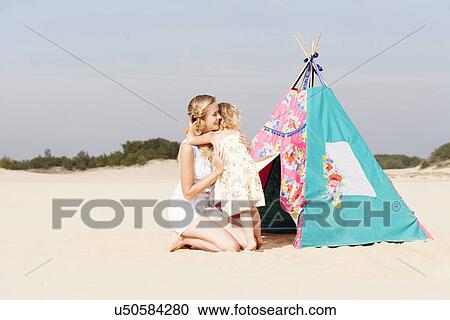 Stock Image - Mother hugging daughter (2-3) on beach. Fotosearch